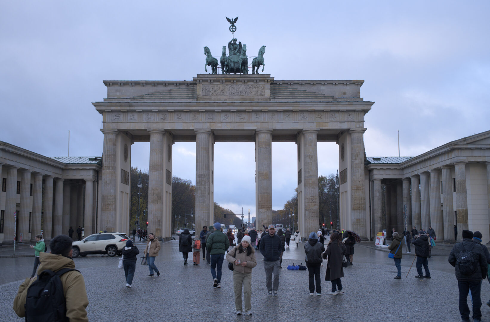 Brandenberg gate, looking west, against an overcast sky, with people wandering around in the foreground.